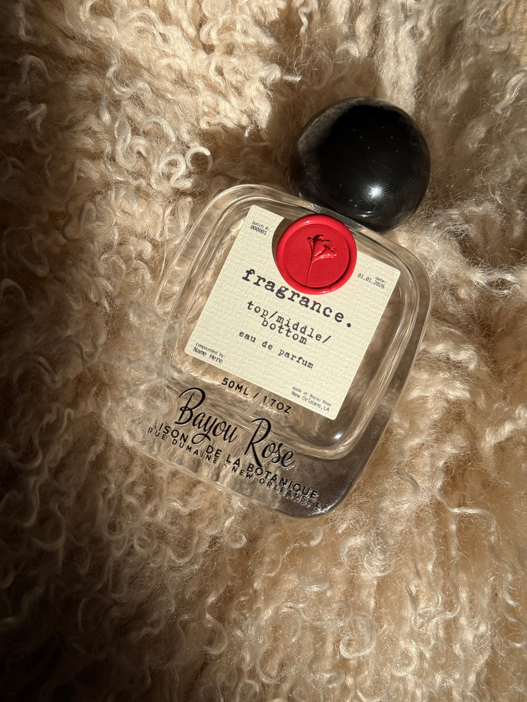 A 50 ml glass perfume bottle with black spherical cap, black text, a paper label and wax seal.
