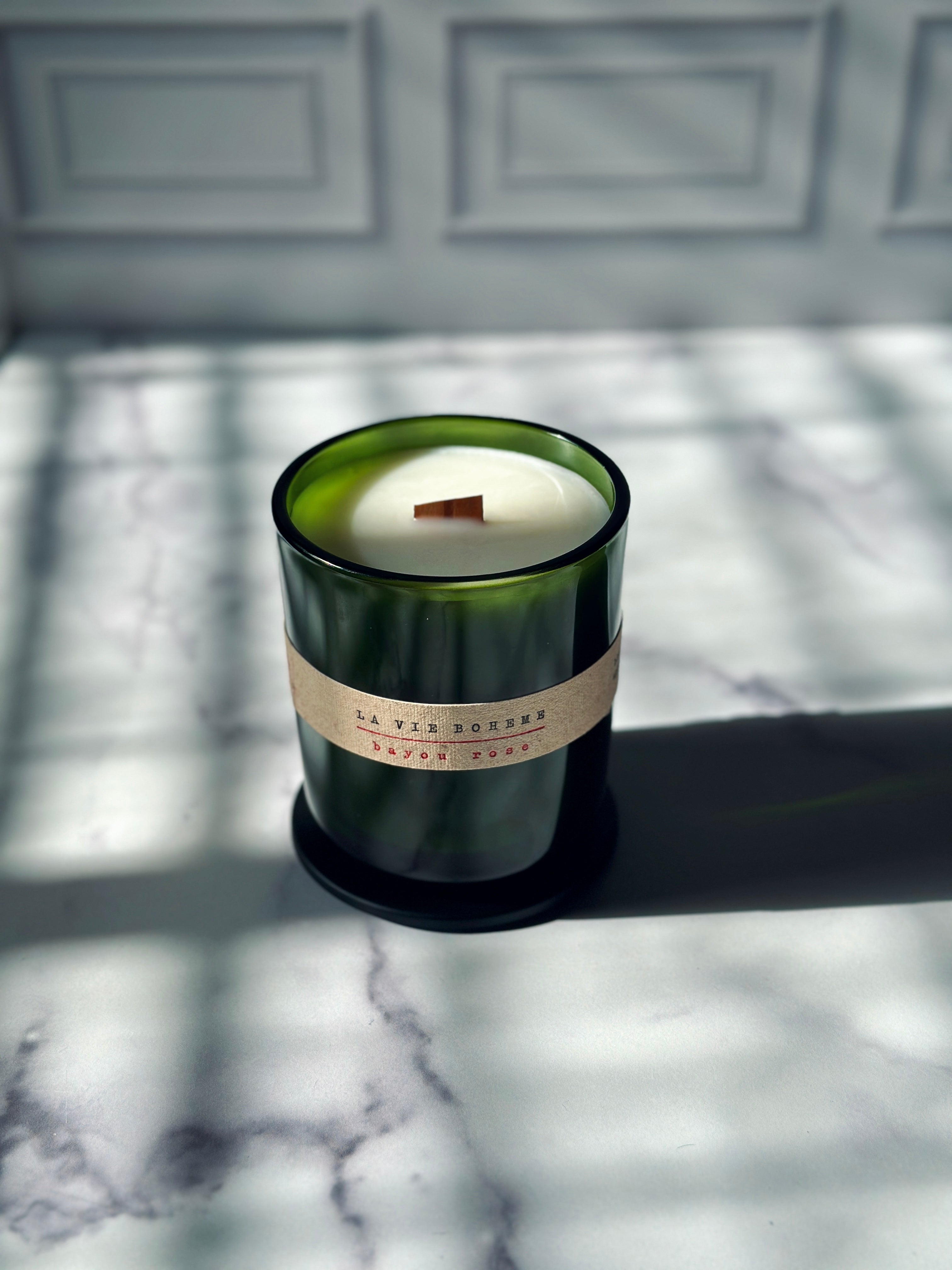 Green glass container candle with wooden wick and black lid on a marble counter