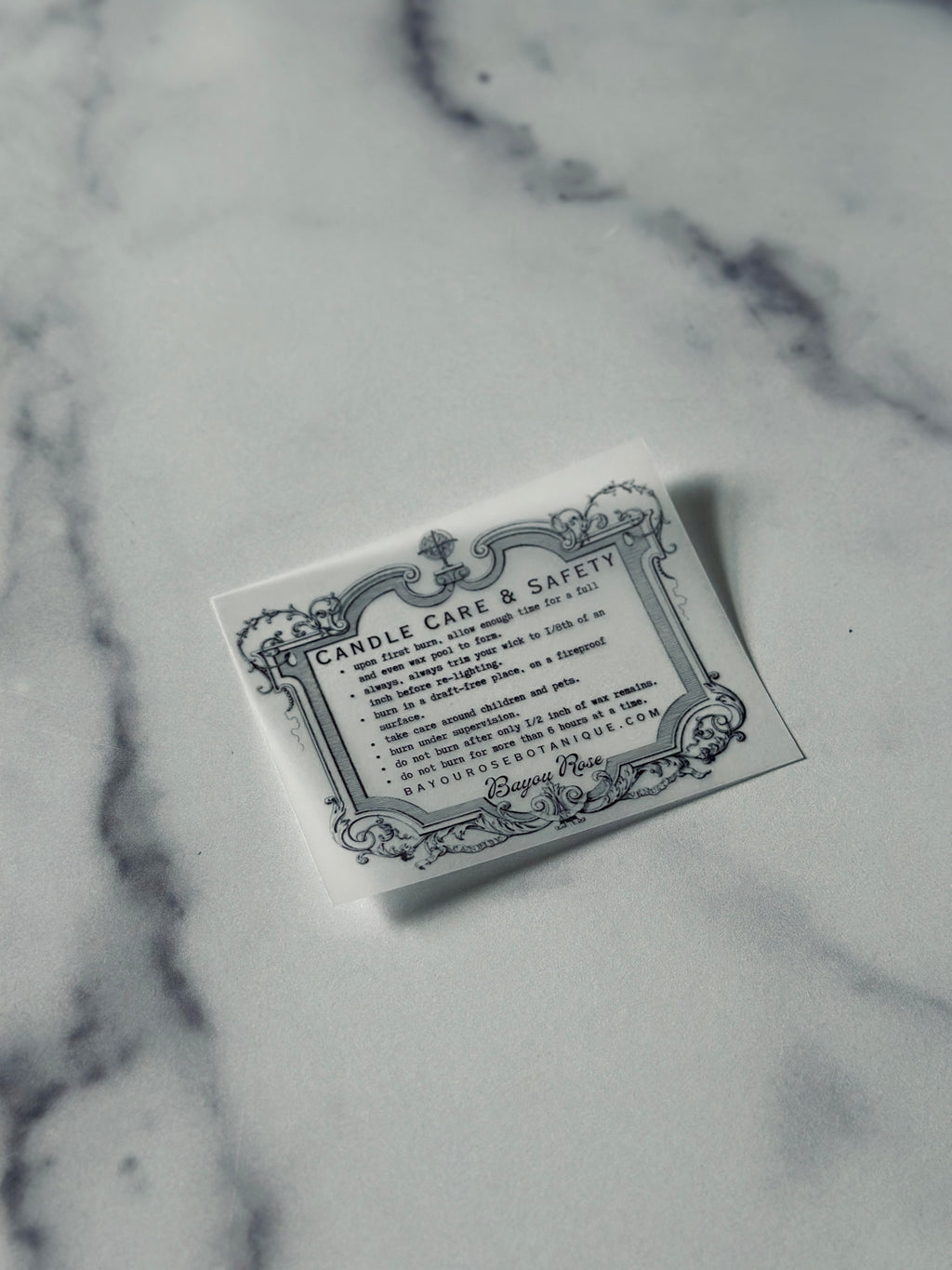 Bayou Rose Botanicals ornate candle care and safety card on marble surface — wooden wick candle care instructions