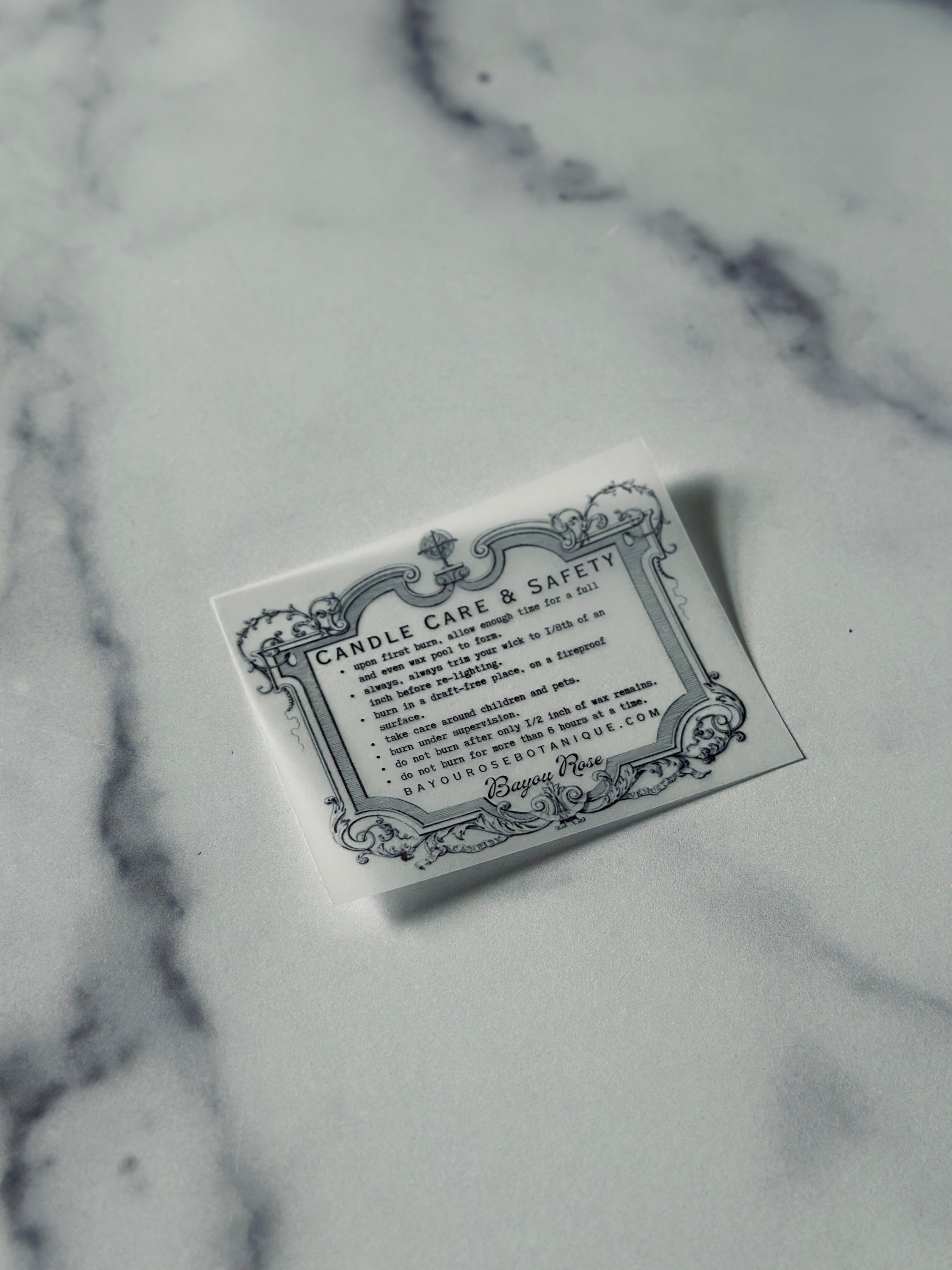 Bayou Rose Botanicals ornate candle care and safety card on marble surface — wooden wick candle care instructions