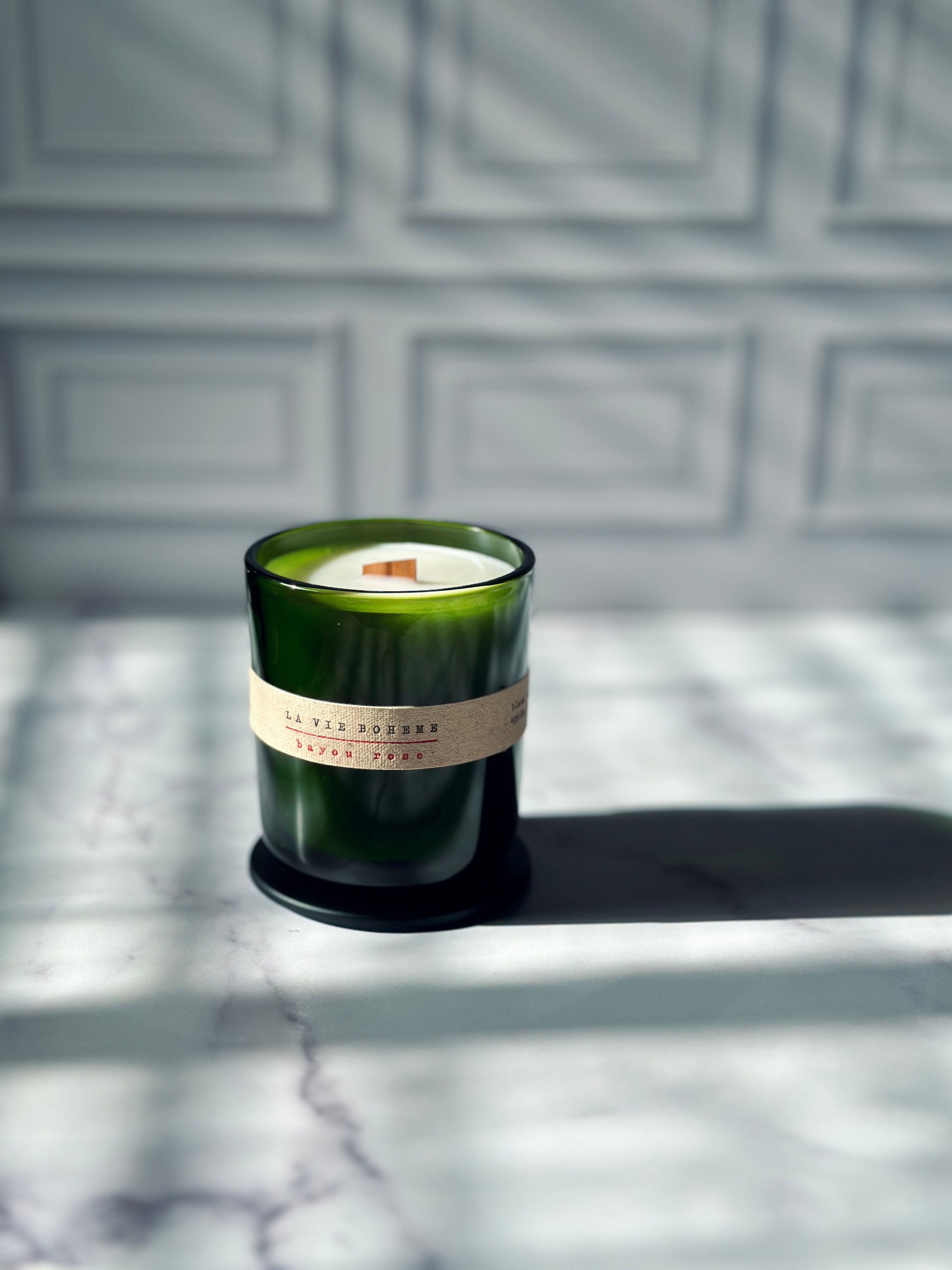 La Vie Boheme luxury scented candle green glass vessel with fabric label and wooden wick, side angle on marble — Bayou Rose French Quarter